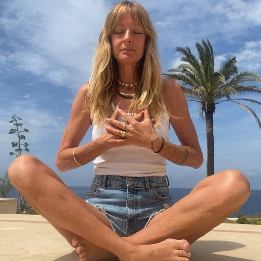 Woman sitting cross-legged on a concrete surface with palm trees and blue sky in the background